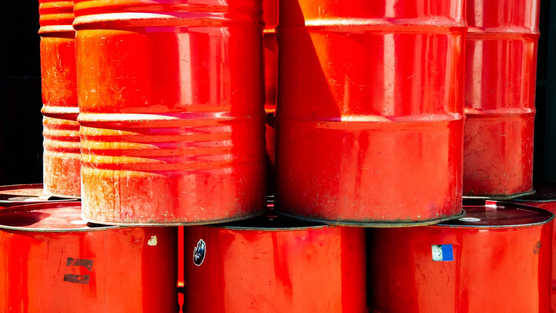 Bright red industrial oil barrels stacked outdoors in daylight, showcasing vivid color and industrial theme.