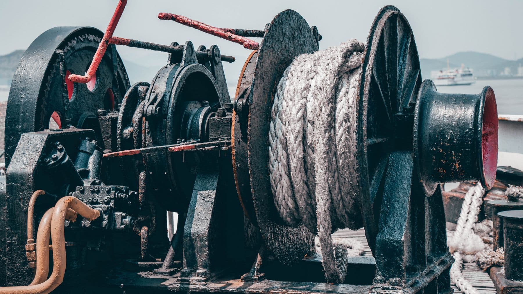 A close-up view of an industrial hydraulic winch on a ship deck with ropes.